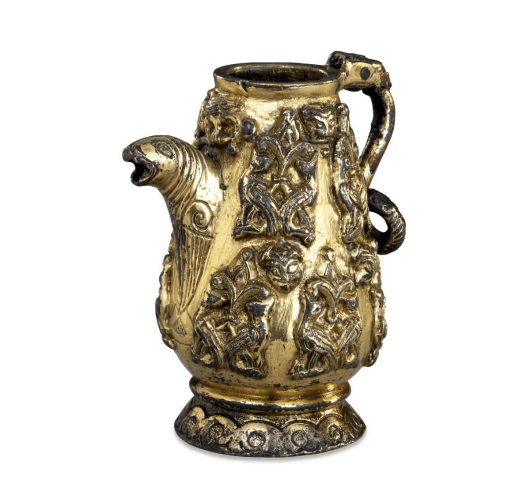 Gilt-copper spouted vessel, still shiny in some places but quite tarnished in others; the handle is formed like a twisted snake, the spout like a winged quadruped, and the sides are decorated with bird and animal designs.