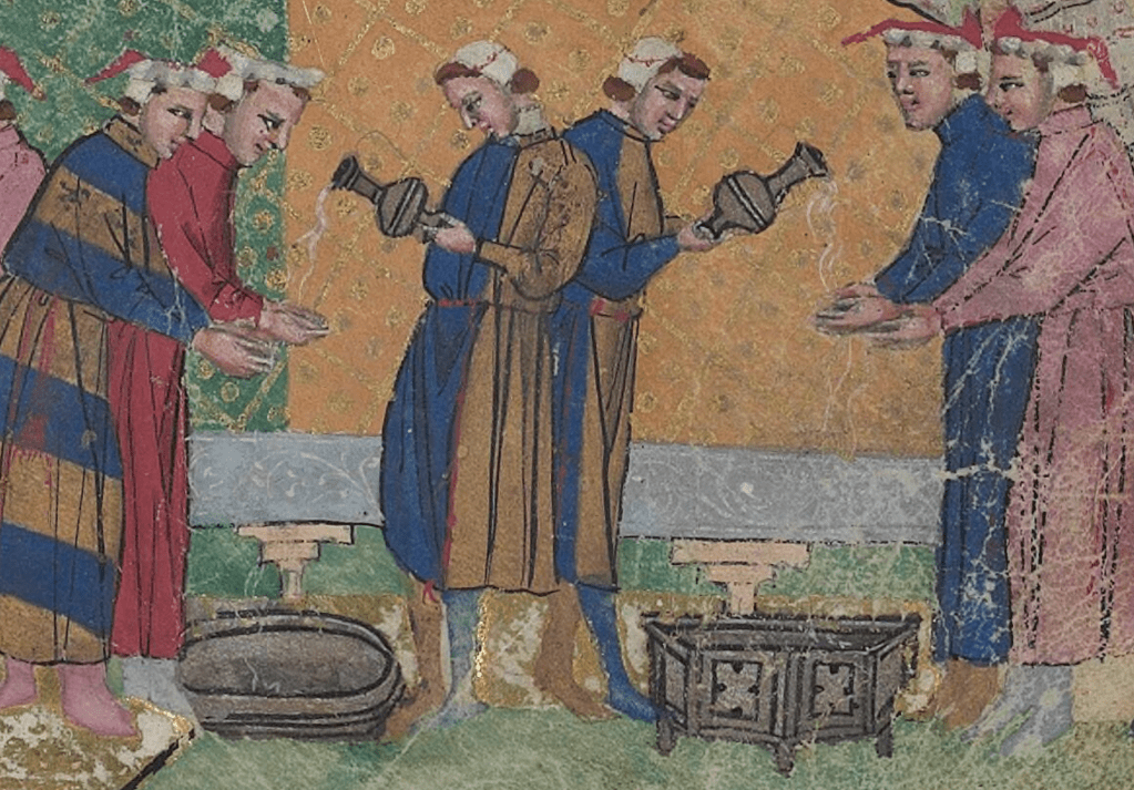 Medieval manuscript image of two servants standing back to back, each pouring water from a vessel onto the hands of a pair of waiting guests; basins sit on the floor to catch the run-off water.