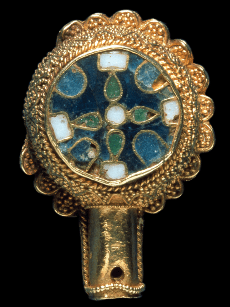 A gold circular object that has a projecting gold cylinder with a hole at the end; the circular part is decorated with gold filigree and a blue, green and white enamel cloisonné design.