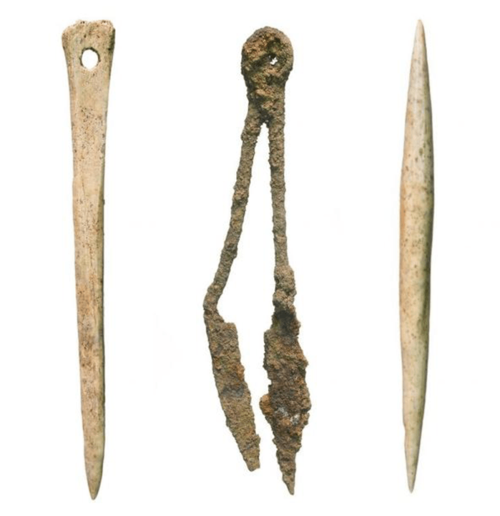 A pointed bone needle, a very rusty two-pronged metal tool, and a bone implement with points on either end.