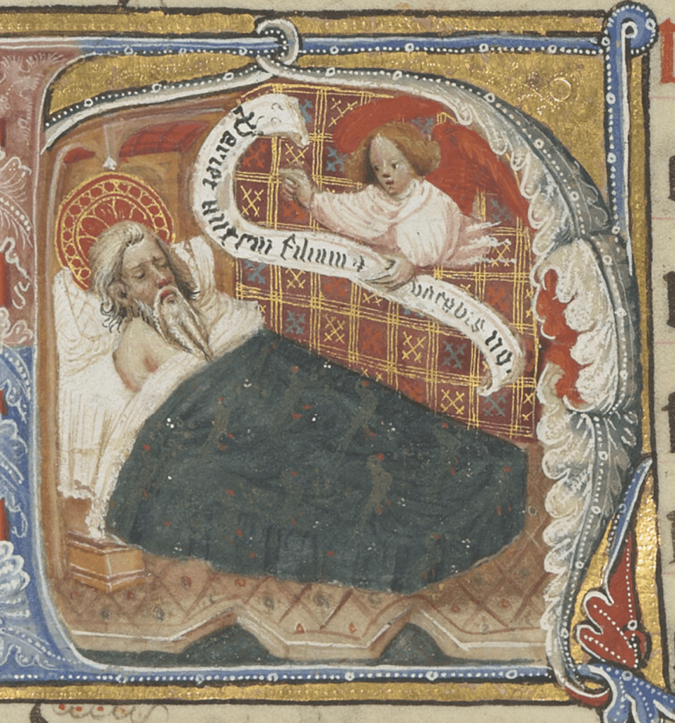 Medieval manuscript image of a bearded man lying in bed beneath a bird-patterned blanket, upper torso naked and exposed; an angel hovers above holding a scroll with Latin text.