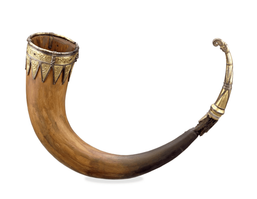 A large plaster drinking horn with silver-gilt and niello mounts that consist of bird head terminal with ribbing and a rim band with human and rosette motifs; triangular mounts run along the lower edge of the rim band.